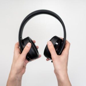 Close-up of hands holding black wireless headphones against a white background.