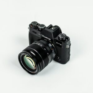 Close-up of a Fujifilm camera with lens on a plain background, showcasing photographic equipment.
